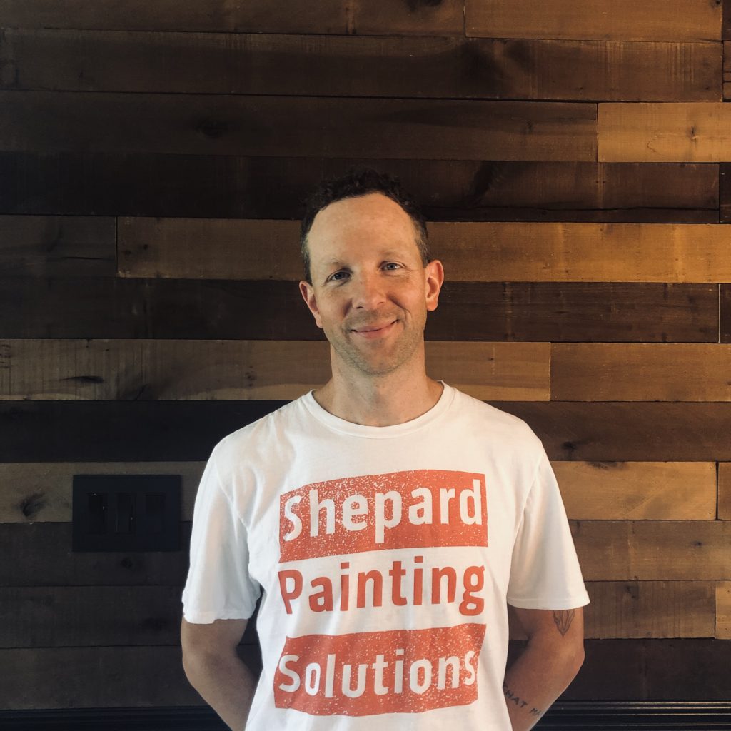 Michael-Shepard-of-Shepard-Painting-Solutions-Smiling-In-Front-Of-A-Decorative-Wood-Wall